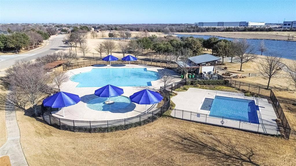 Community pool area featuring two distinct swimming basins, concrete decking, metal perimeter fencing, and an open-air pavilion