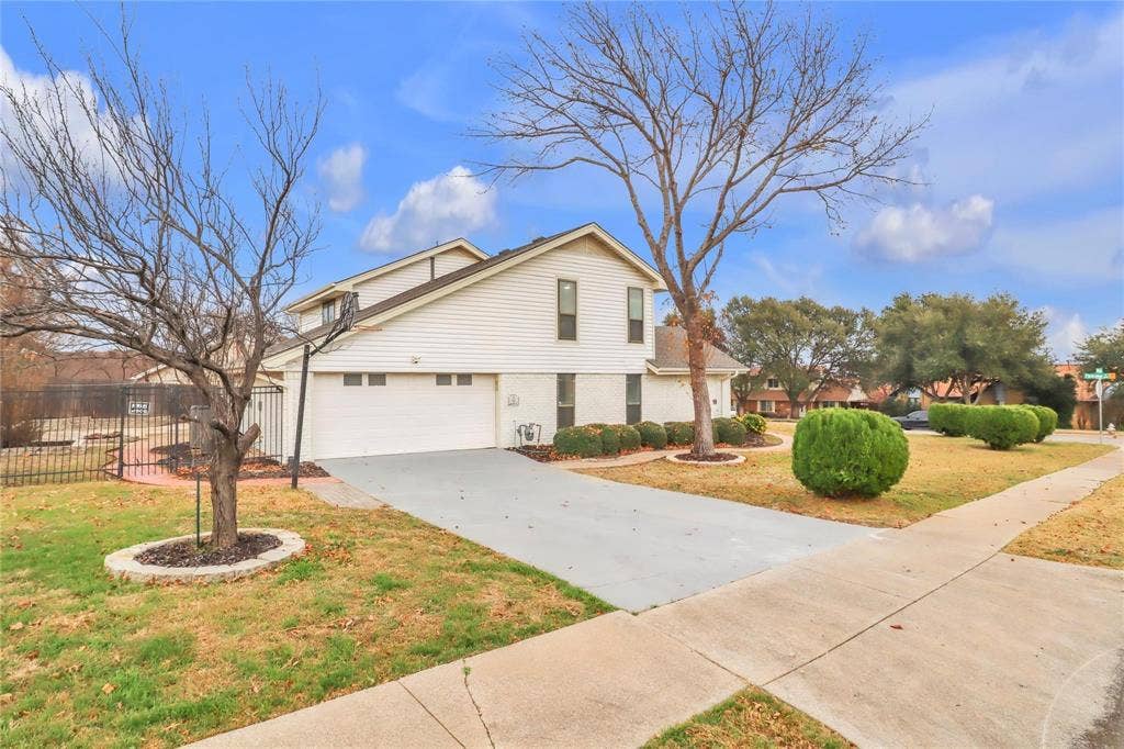 600 Flintridge Court, Irving, TX 75038 Two-story residence featuring light-colored horizontal siding, brick lower-level exterior, an attached two-car garage, and mature landscaping