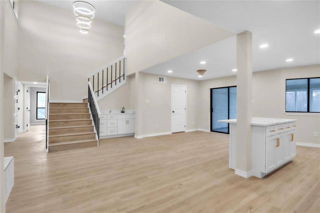 600 Flintridge Court, Irving, TX 75038 Open-concept interior featuring wood-finish flooring, a double-height ceiling with a multi-ring chandelier, a staircase with matte black metal balusters, and a central island with white cabinetry and quartz-style countertop