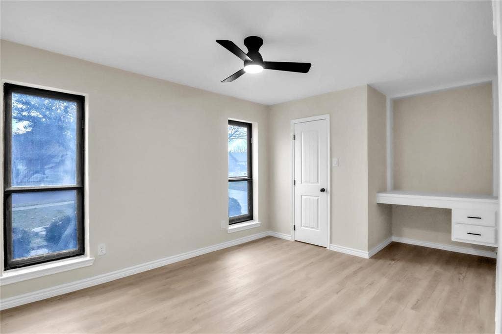 600 Flintridge Court, Irving, TX 75038 Neutral wall tones with wood-finish flooring, dual windows with black frames, a contemporary ceiling fan with integrated lighting, a solid-core interior door, and a built-in desk with dual storage drawers