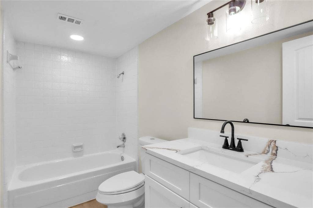 600 Flintridge Court, Irving, TX 75038 White vanity with stone-patterned countertop, under-mount sink, matte black widespread faucet, rectangular mirror with thin black frame, and tiled tub-shower combination