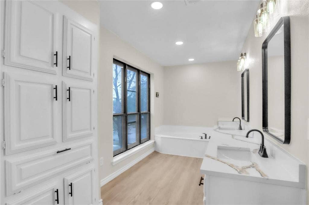 600 Flintridge Court, Irving, TX 75038 Double vanity featuring white cabinetry, solid-surface countertops, and matte black fixtures, paired with a built-in soaking tub, tall floor-to-ceiling cabinetry, and recessed lighting