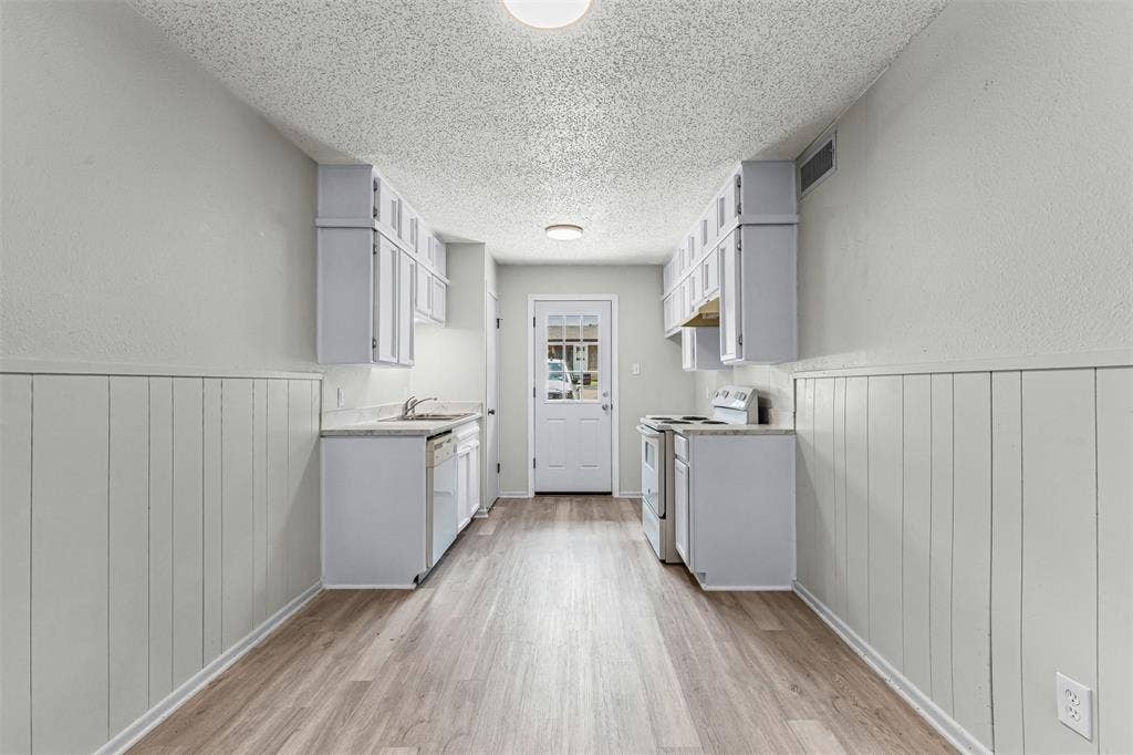 Kitchen with white appliances, light wood-type flooring, a textured ceiling, light countertops, and a wainscoted wall