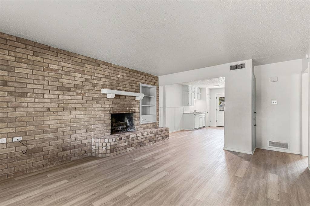 Unfurnished living room featuring a textured ceiling, light wood-style floors, brick wall, and a brick fireplace