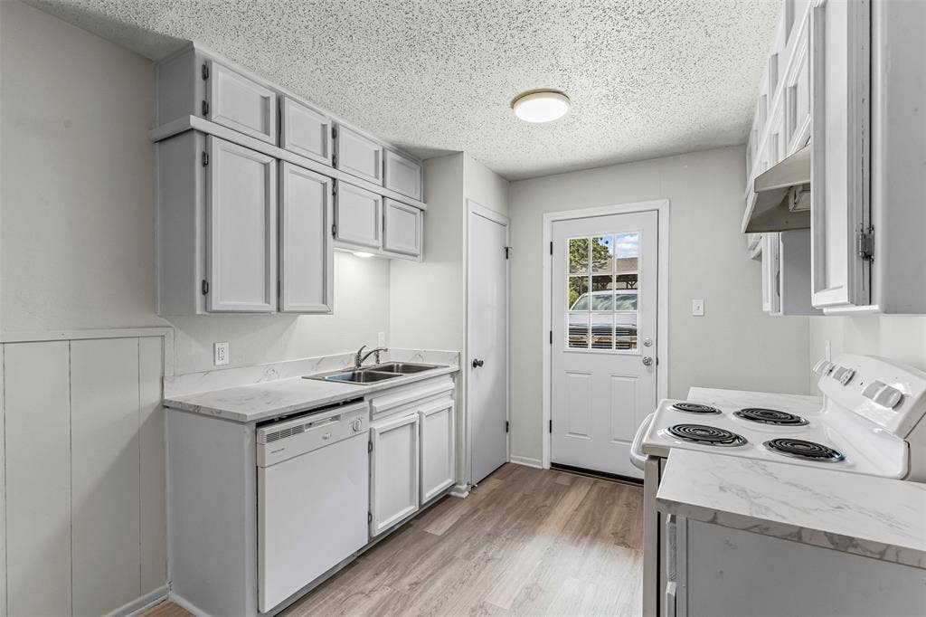 Kitchen with white appliances, light wood-style floors, a textured ceiling, and under cabinet range hood