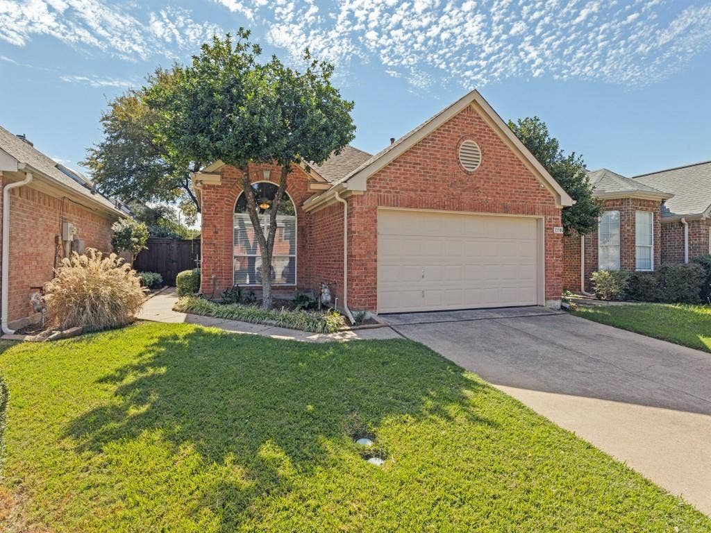 2206 Jasmine Lane, Garland, TX 75044 Brick exterior featuring a front-facing attached garage, arched window, gable roofline, and concrete driveway