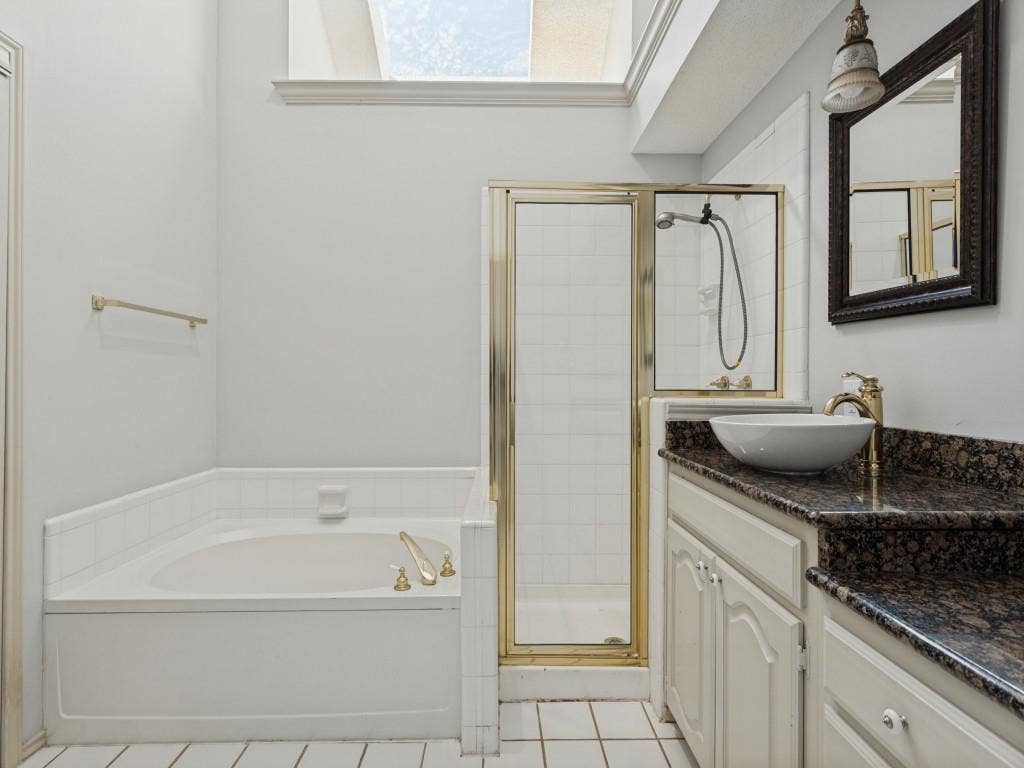 2206 Jasmine Lane, Garland, TX 75044 Bathroom featuring a deep soaking tub, glass-enclosed shower with metal framing, vanity with a stone-finish countertop, vessel sink, and overhead skylight