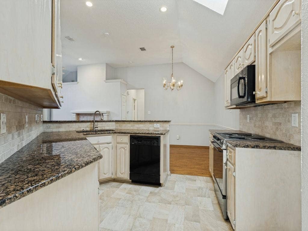 2206 Jasmine Lane, Garland, TX 75044 Kitchen featuring light-toned cabinetry, granite countertops, tiled backsplash, built-in black appliances, and a vaulted ceiling with a skylight
