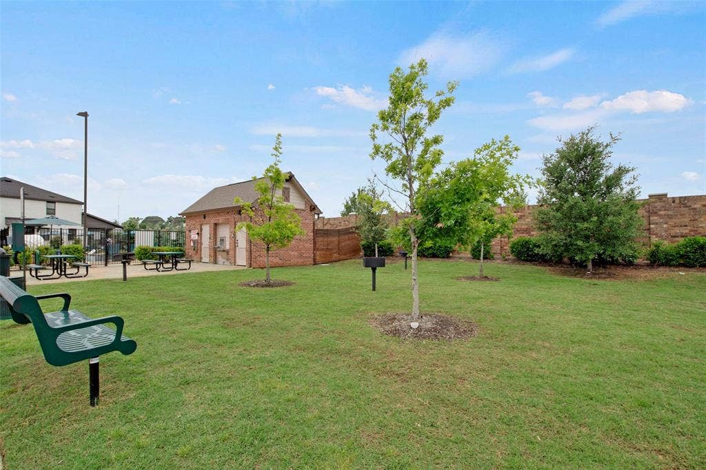 Expansive green space featuring a brick structure, mature trees, built-in metal pedestal grills, and perimeter masonry wall
