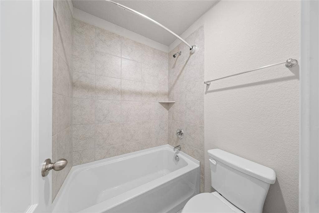 Bathroom featuring a white acrylic bathtub, neutral-toned wall tile surround, built-in corner soap ledge, chrome finish plumbing fixtures, and a wall-mounted towel bar