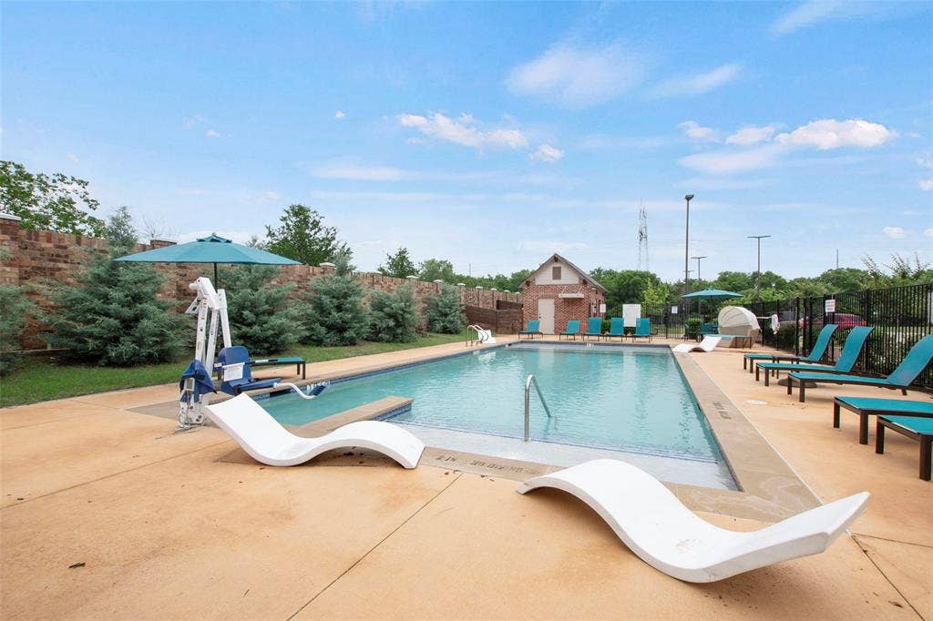 Outdoor swimming pool featuring a concrete deck, brick perimeter wall, and built-in pool lift