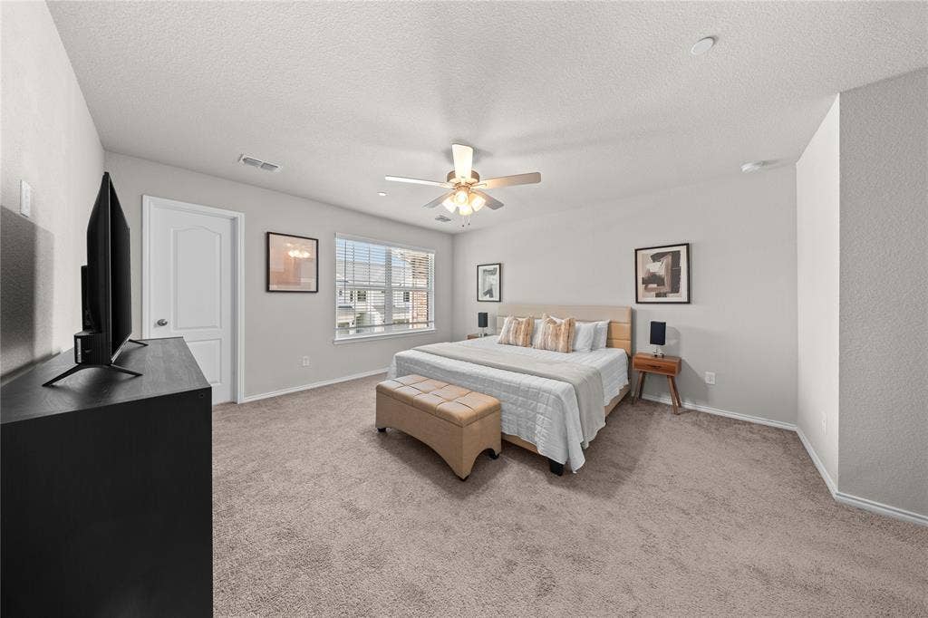 Spacious interior featuring neutral wall tones, wall-to-wall carpeting, a multi-blade ceiling fan with integrated light fixture, and a white six-panel door