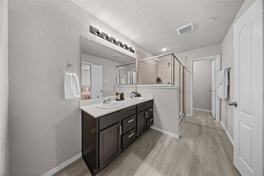 Double vanity featuring dark cabinetry, solid-surface countertop, dual recessed sinks, and a full-width mirror