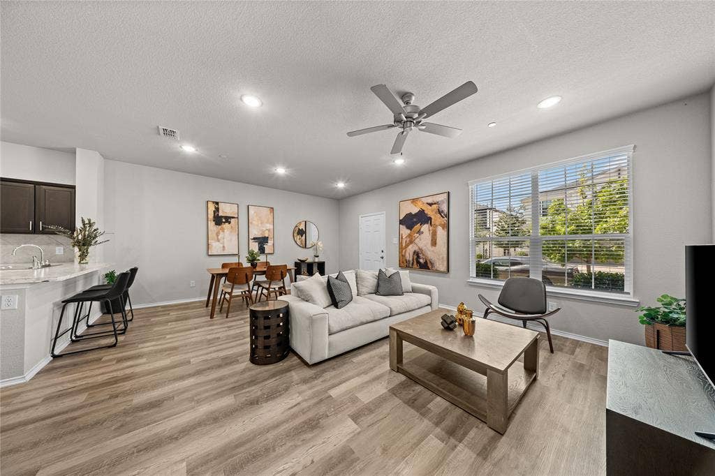 Open-concept living space featuring wood-finish flooring, recessed lighting, a ceiling fan, and large windows with horizontal blinds