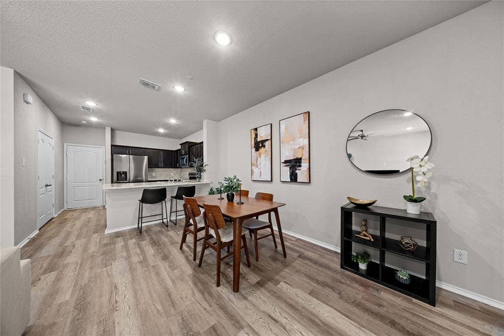 Open-concept kitchen featuring dark wood cabinetry, stainless steel appliances, and a quartz breakfast bar with pendant lighting, complemented by wood-finish flooring throughout