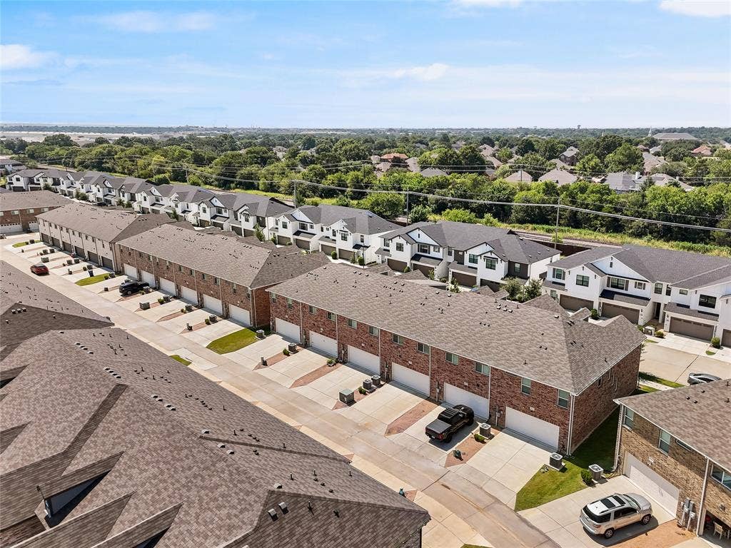 Aerial perspective of townhome community featuring brick and multi-tone masonry facades, pitched shingle roofing, and attached multi-car garages with concrete driveways