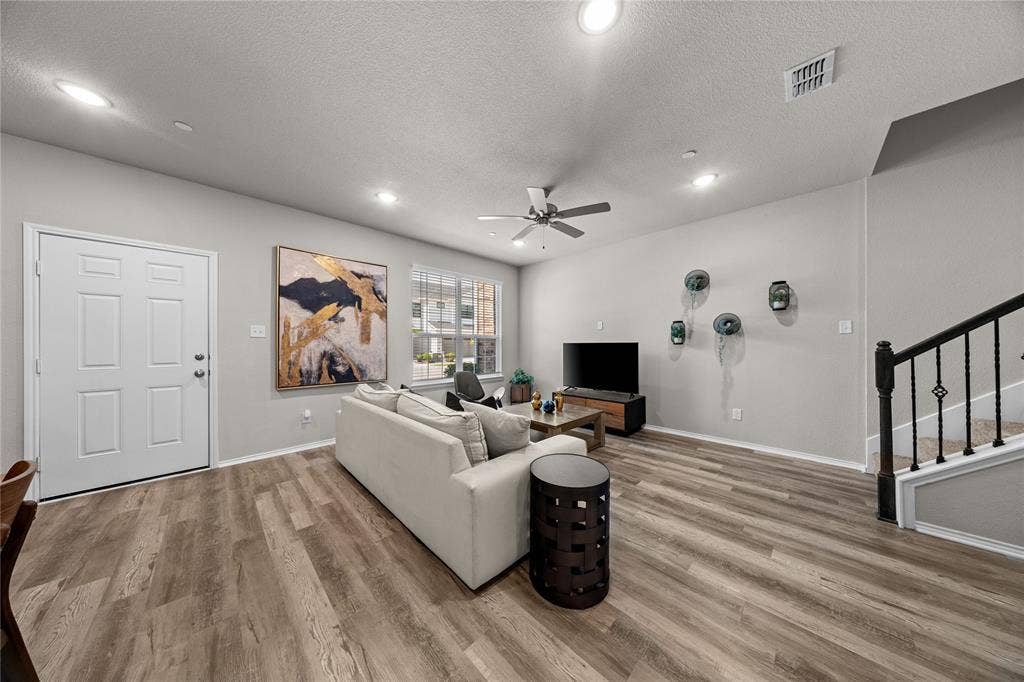 Open-concept interior featuring wood-finish flooring, recessed lighting, a ceiling fan, and a staircase with a black metal balustrade
