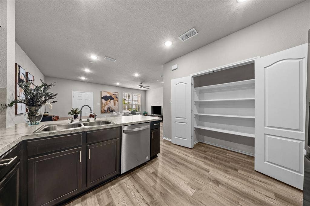 Kitchen featuring dark cabinetry, stone-finish countertops, stainless steel dual-basin sink, stainless steel dishwasher, and pantry with built-in shelving