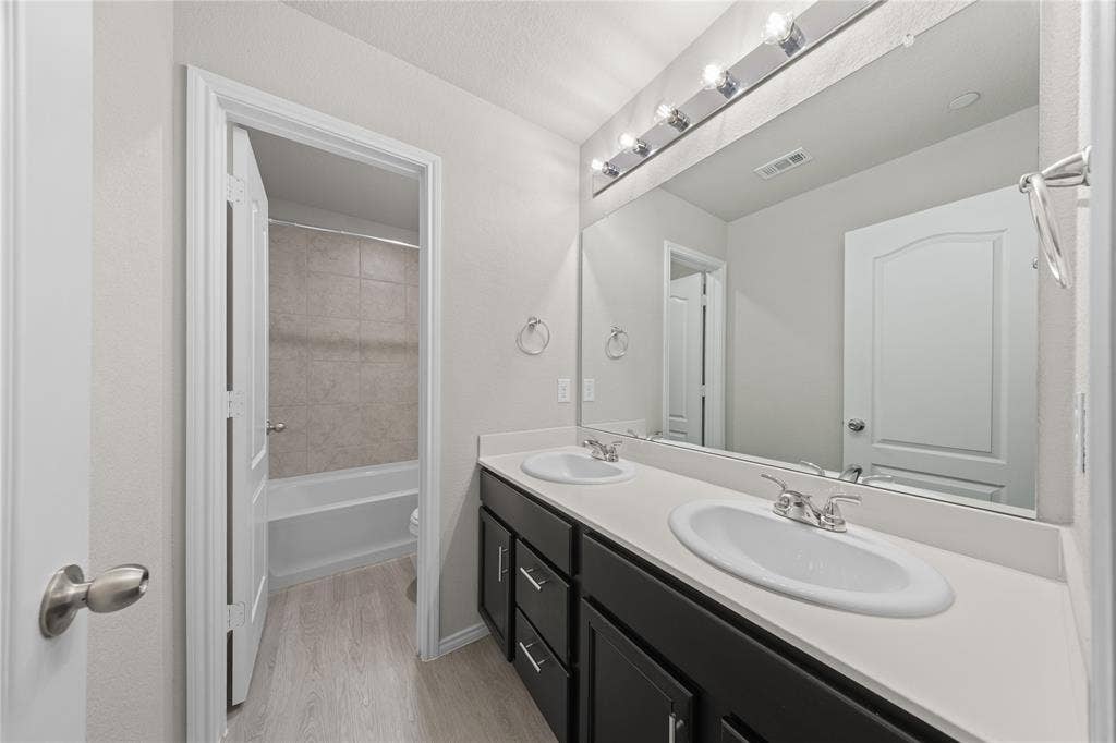Double vanity featuring a light-toned countertop, dual integrated sinks, dark-finish cabinetry, and a full-width mirror with integrated lighting