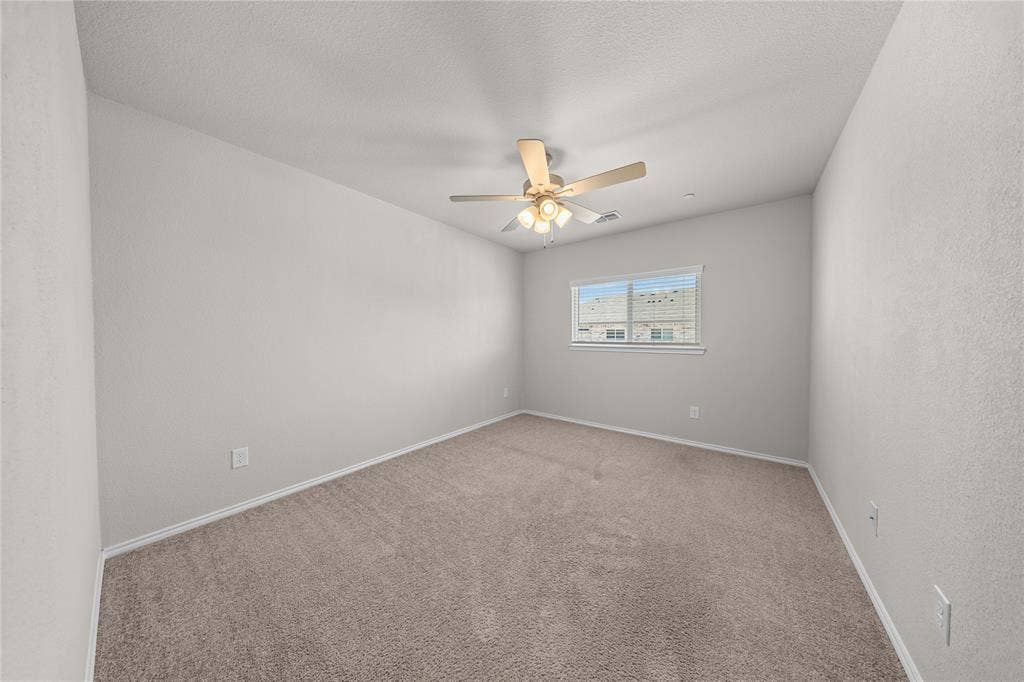 Neutral-toned interior room featuring wall-to-wall carpeting, a ceiling fan with integrated light fixture, and a single-pane window