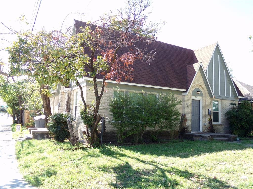 902 Centre Street, Dallas, TX 75208 Tudor-style exterior featuring light-colored brick masonry, steeply pitched rooflines, prominent decorative timbering, an arched entryway, and a concrete front porch