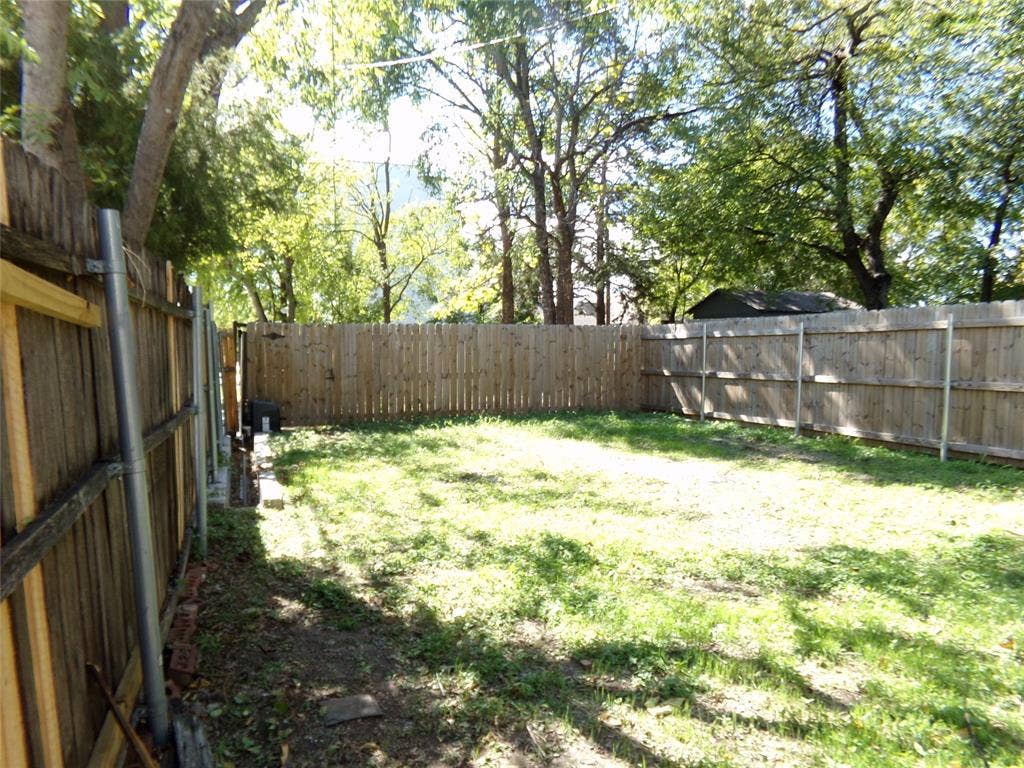 902 Centre Street, Dallas, TX 75208 Backyard area featuring a wood fence, mature trees, and open lawn space