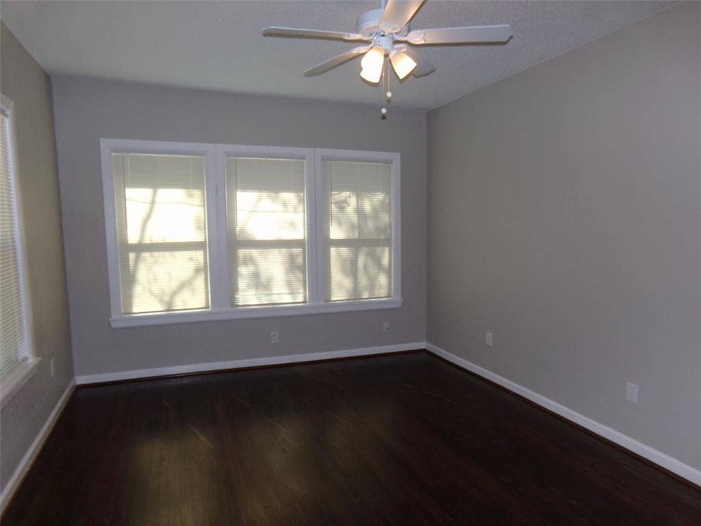 902 Centre Street, Dallas, TX 75208 Room featuring wood-finish flooring, a neutral wall color palette, a triple-pane window configuration, and a ceiling-mounted light fixture with a multi-blade fan