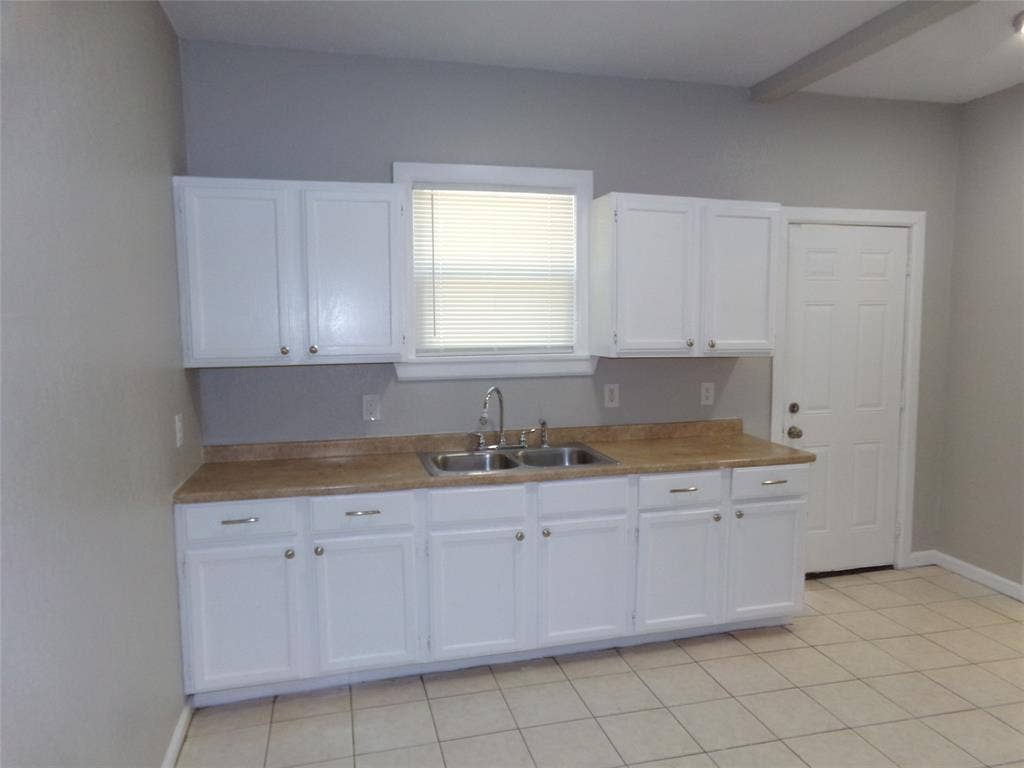 902 Centre Street, Dallas, TX 75208 Kitchen featuring white shaker-style cabinetry, neutral-toned solid surface countertops, stainless steel dual-basin sink with arched faucet, and light ceramic tile flooring