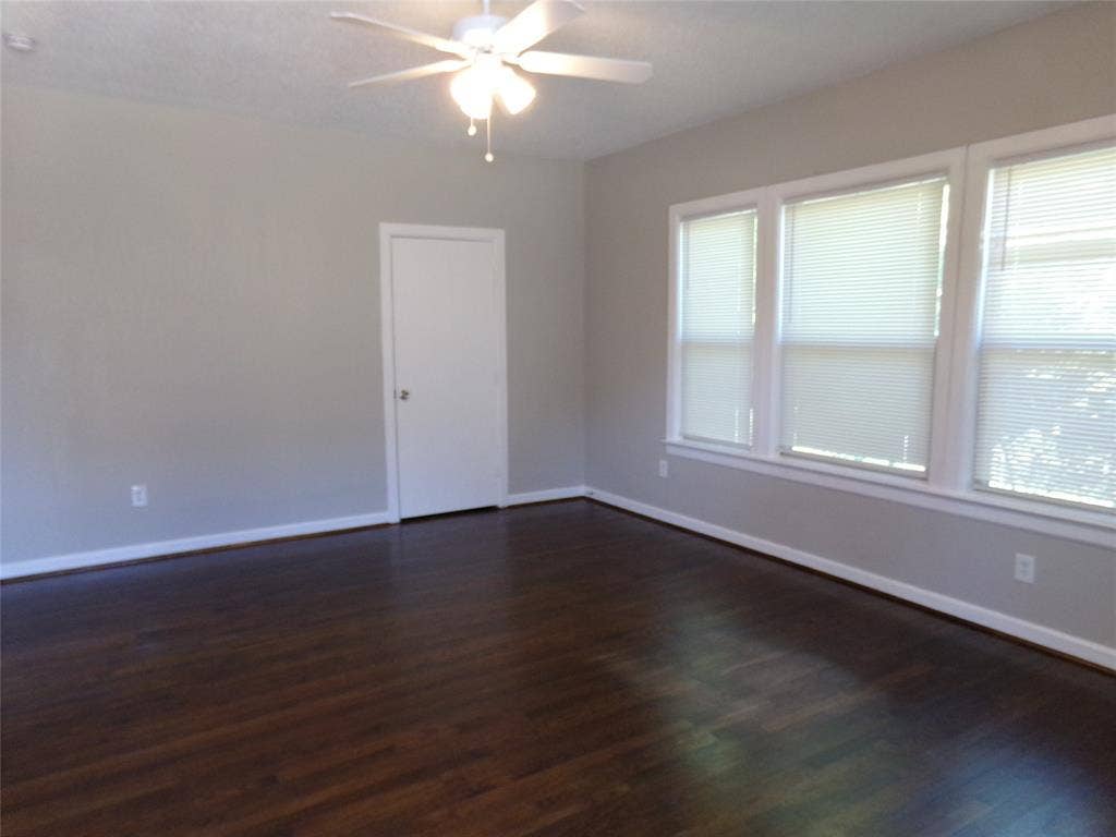 902 Centre Street, Dallas, TX 75208 Neutral-toned interior space featuring dark wood-finish flooring, three large windows with horizontal blinds, and a central ceiling-mounted light fixture