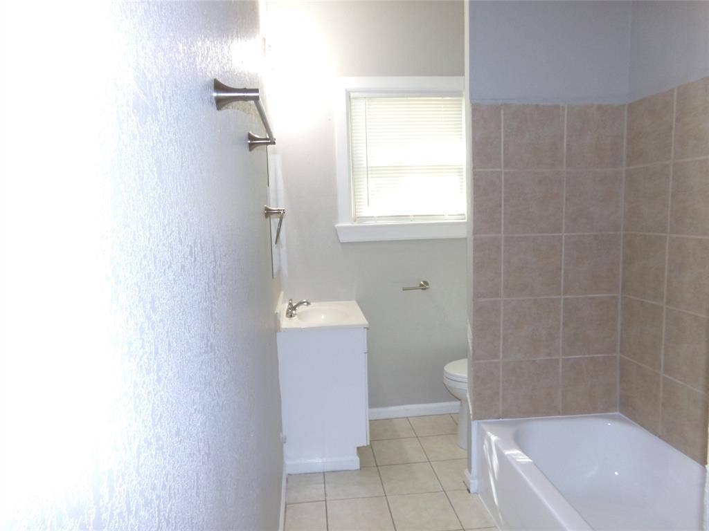902 Centre Street, Dallas, TX 75208 Bathroom featuring a neutral-tone tile tub surround, white pedestal vanity, ceramic tile flooring, and wall-mounted metal hardware