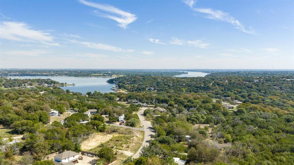 Aerial perspective showcasing expansive water frontage, dense mature tree canopy, and established neighborhood topography