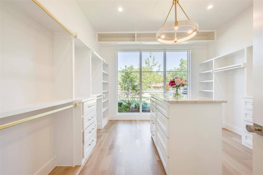 Light filled primary closet with built in dresser island and modern lighting