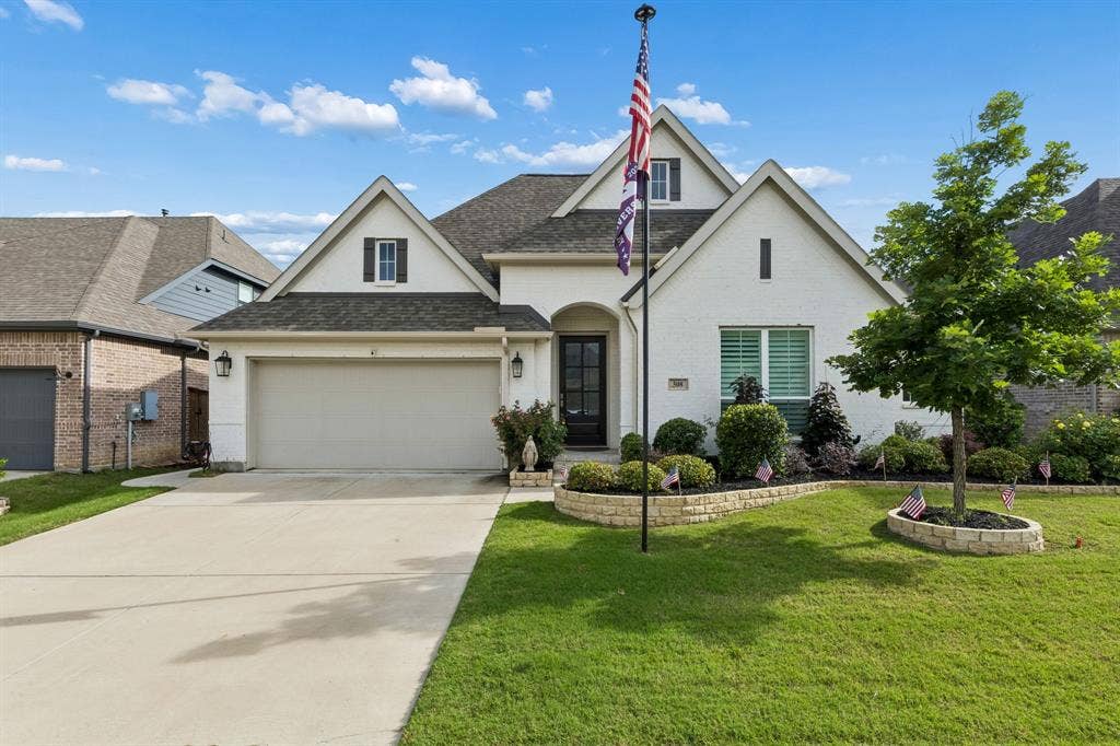 Brick exterior featuring multiple gables, a covered entryway, concrete driveway, and stone-bordered landscaping