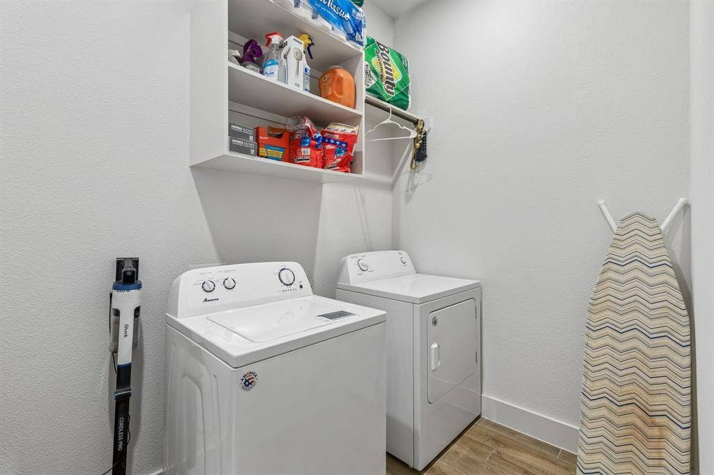 Laundry area featuring wood-finish flooring, white upper shelving, and a wall-mounted hanging rod