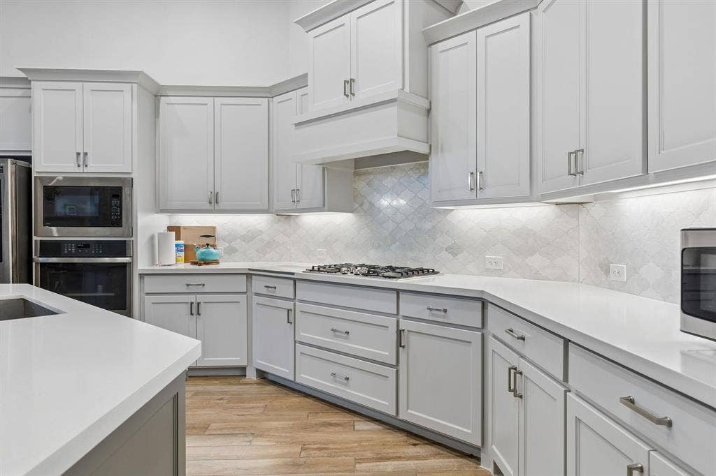 Kitchen featuring white shaker-style cabinetry, quartz countertops, geometric tile backsplash, stainless steel built-in double wall oven, and wood-finish flooring