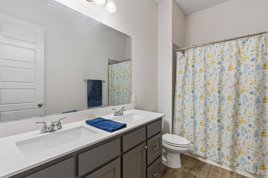 Double vanity featuring a white solid-surface countertop, dual drop-in sinks with polished chrome faucets, grey shaker-style cabinetry, and wood-finish flooring