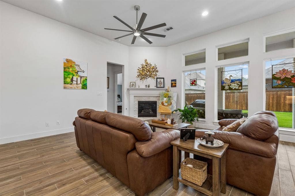 High ceilings featuring a multi-blade ceiling fan, wood-finish flooring, fireplace with a stone-surround mantel, and oversized windows with transom glass