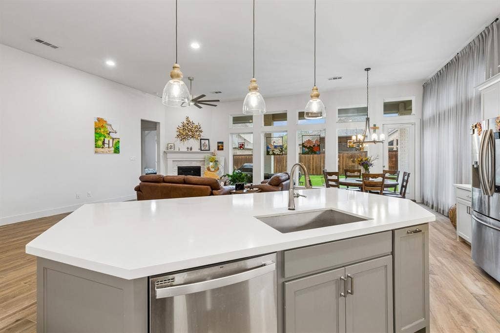 Kitchen island featuring a white countertop, undermount stainless steel sink, and gray cabinetry, illuminated by three pendant lights