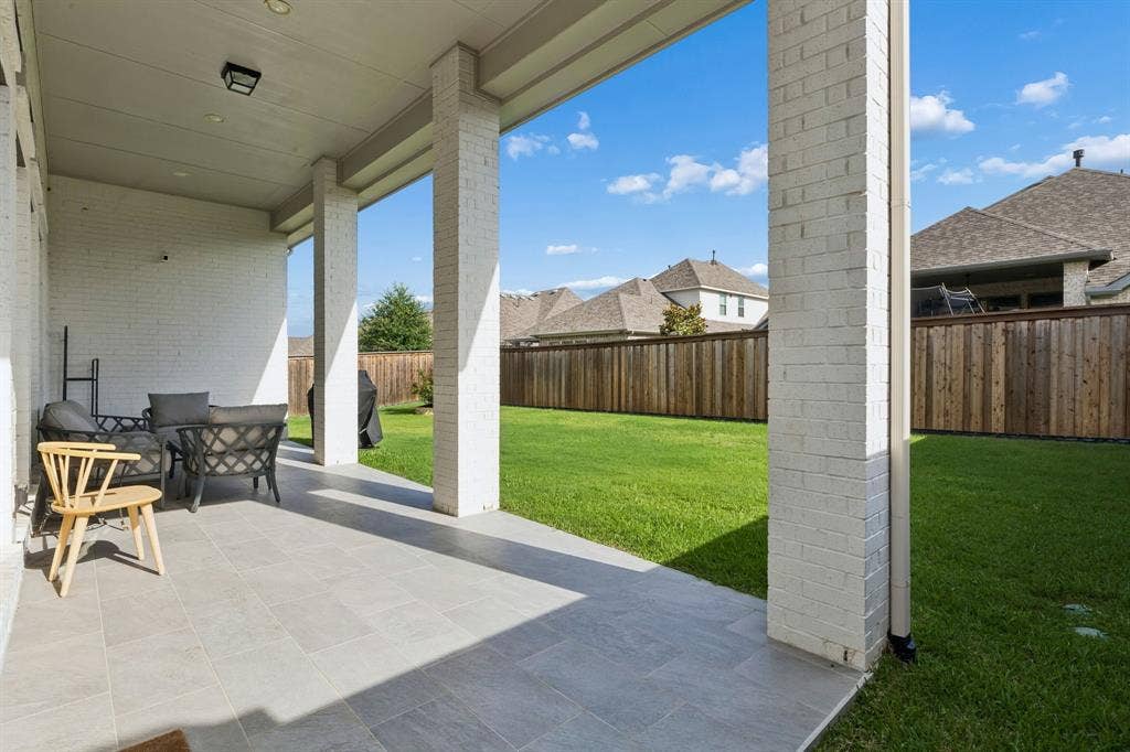 Covered patio with neutral tile flooring, white painted brick columns, and expansive fenced backyard with a grass lawn