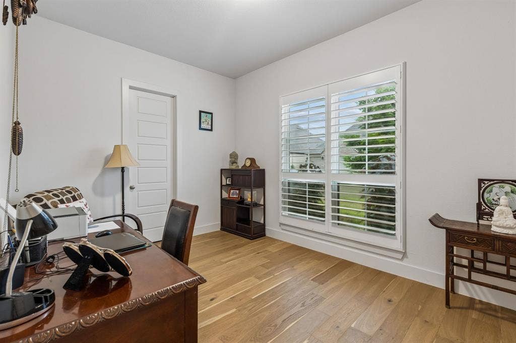 Interior room featuring wood-finish flooring, white walls, and large windows with integrated plantation-style shutters