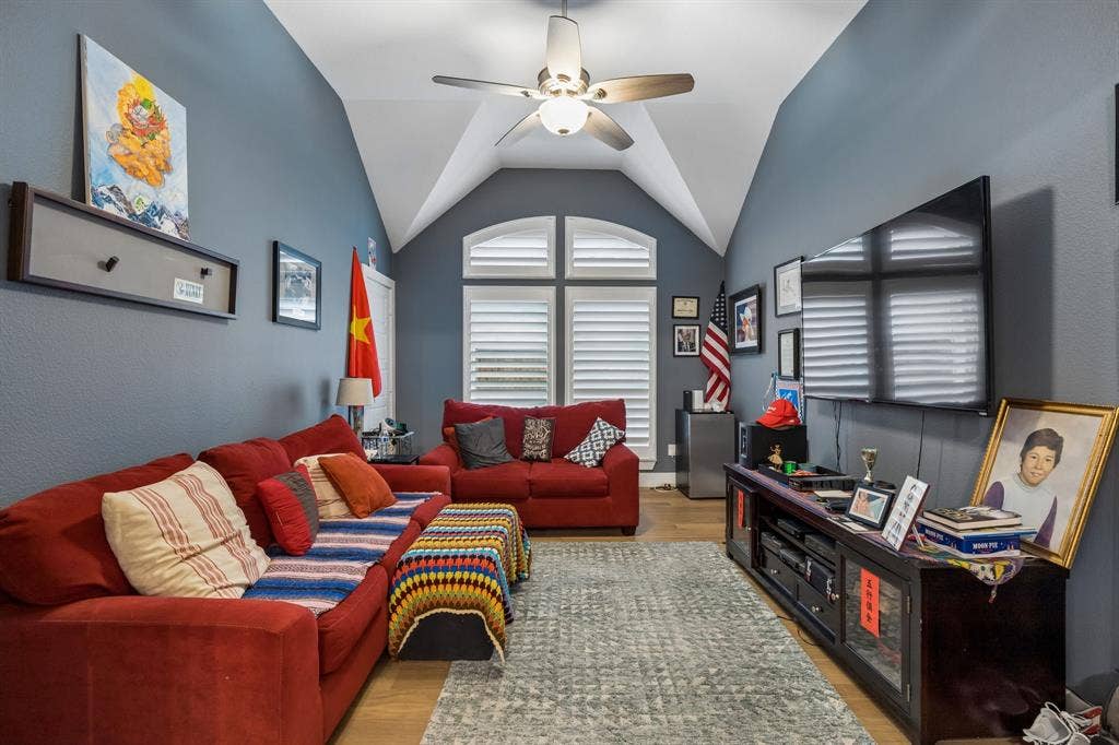Vaulted ceilings, wood-finish flooring, dual-arched windows with plantation shutters, and a central ceiling fan with integrated lighting