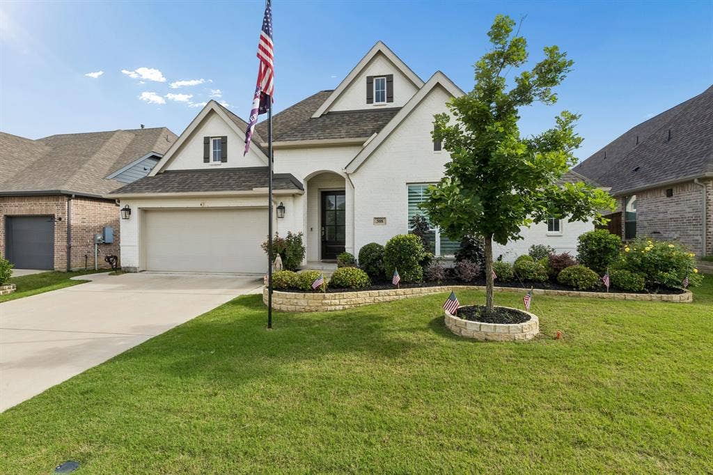 Brick exterior residence featuring a multi-gabled roofline, concrete driveway, attached two-car garage, and tiered stone garden beds