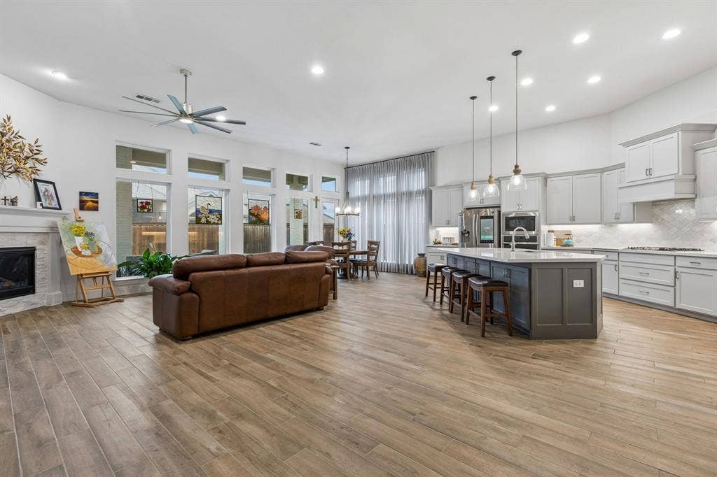 Open-concept living space featuring wood-finish flooring, vaulted ceilings, a fireplace with stone surround, a central island with countertop seating, and recessed lighting