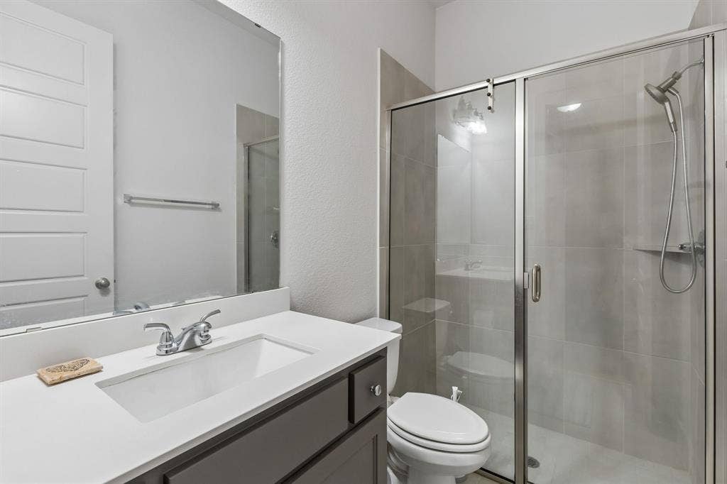 Bathroom featuring a vanity with a white countertop and rectangular undermount sink, large wall-mounted mirror, and walk-in shower with tiled surround and glass sliding enclosure