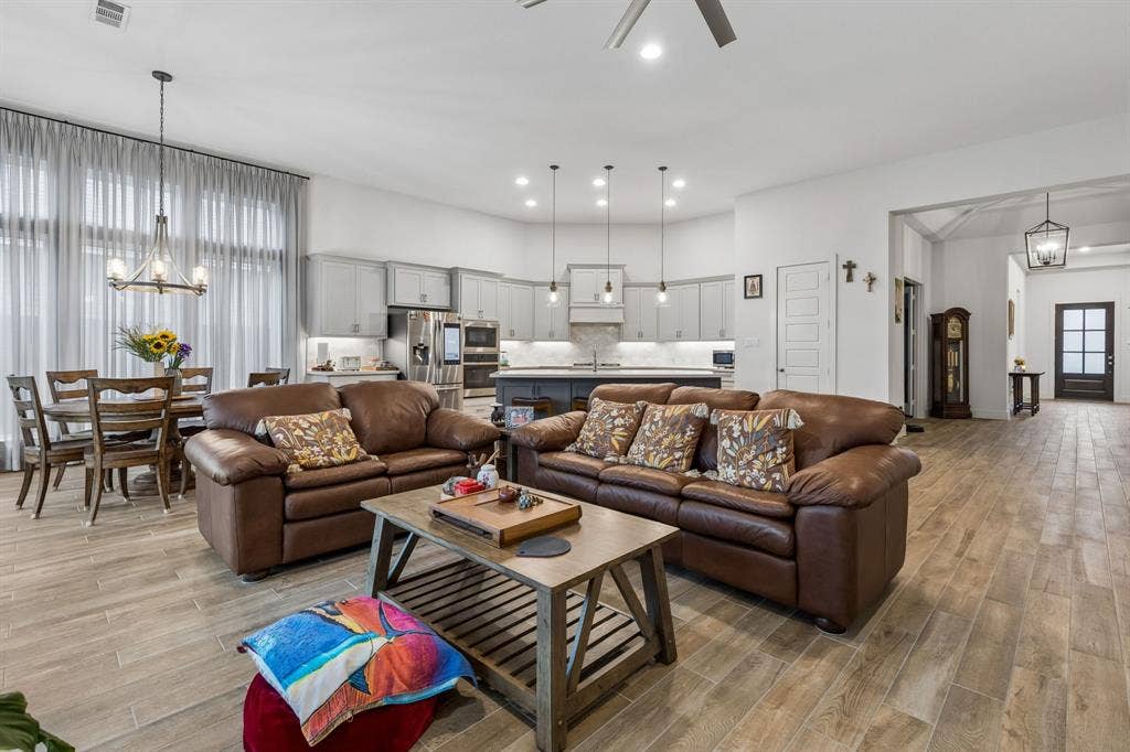 Open-concept interior featuring wood-finish tile flooring, custom cabinetry with a central island, stainless steel built-in appliances, recessed lighting, and multi-pendant illumination