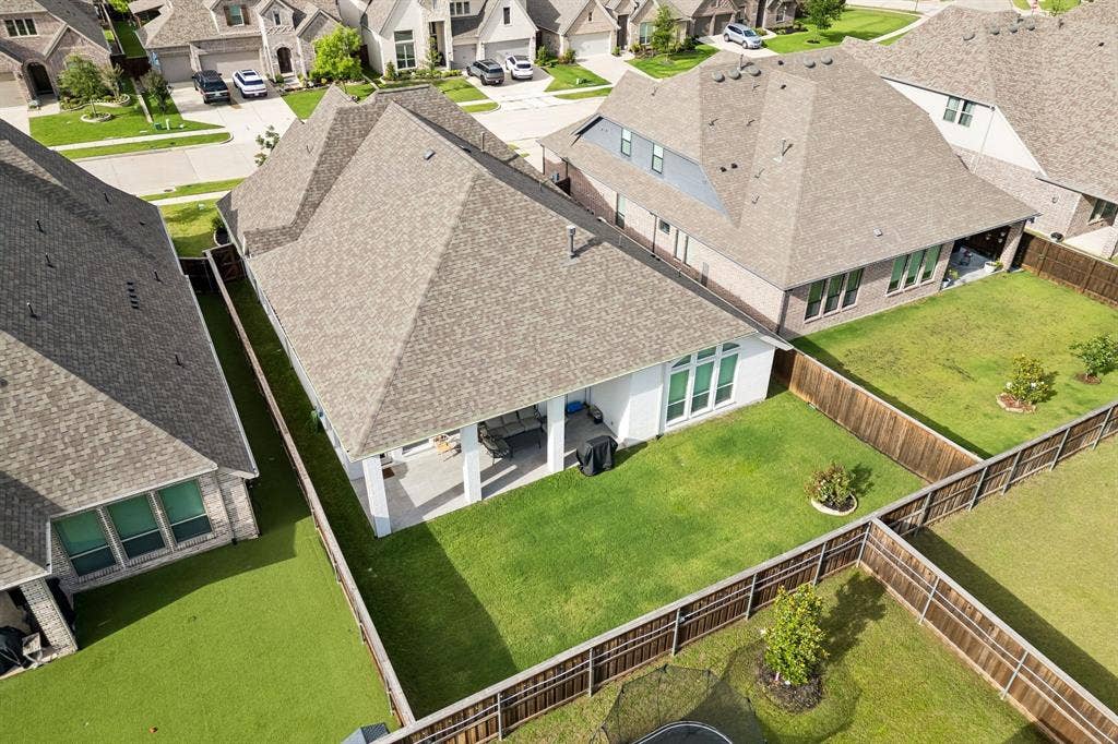 Rear exterior featuring a covered patio, shingle roof, white masonry siding, and a fenced backyard with a lawn
