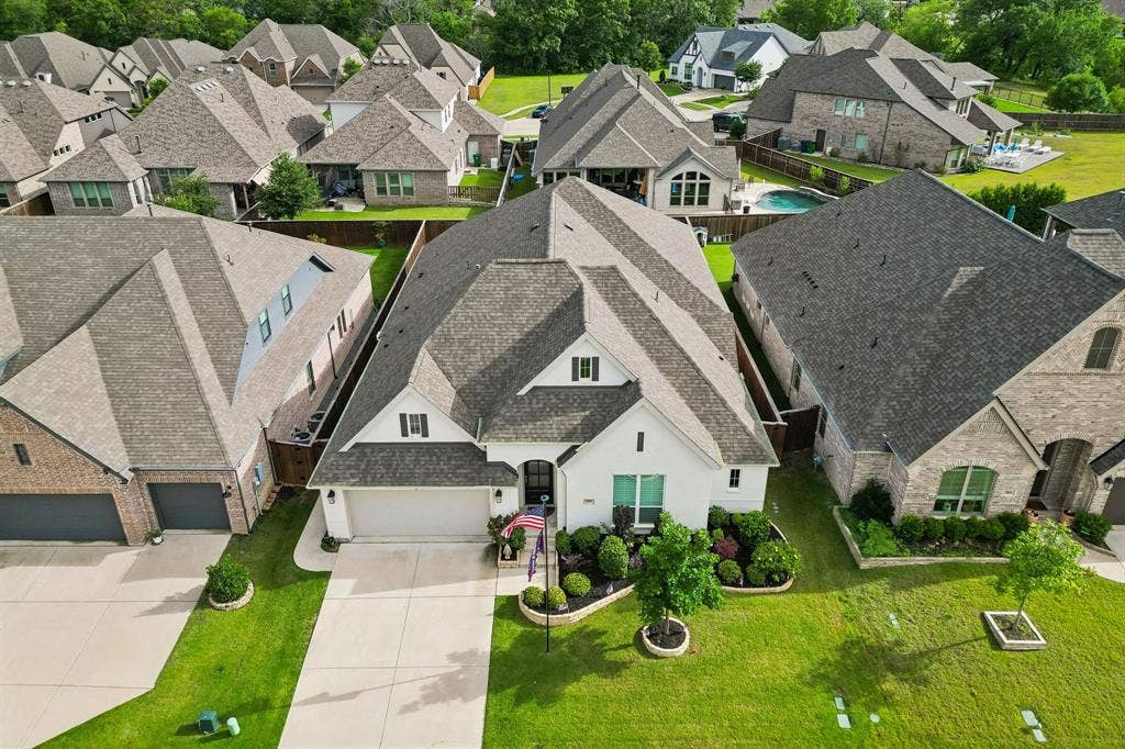 White masonry exterior featuring a multi-gabled roof, two-car garage, and manicured front lawn with established shrubbery
