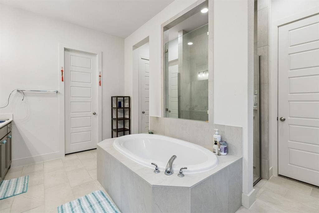 Oval soaking tub with a tiled surround, glass-enclosed shower, polished metal fixtures, and multiple paneled doors