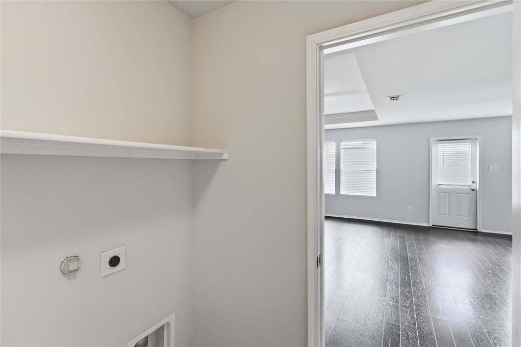 Utility space featuring a built-in shelf and dedicated hookups, highlighting dark-toned wood-finish flooring and an exterior door in the visible room