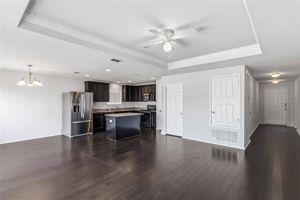 Open concept interior featuring dark wood-finish flooring, a tray ceiling with a center fan, a kitchen island, built-in dark cabinetry, and stainless steel appliances